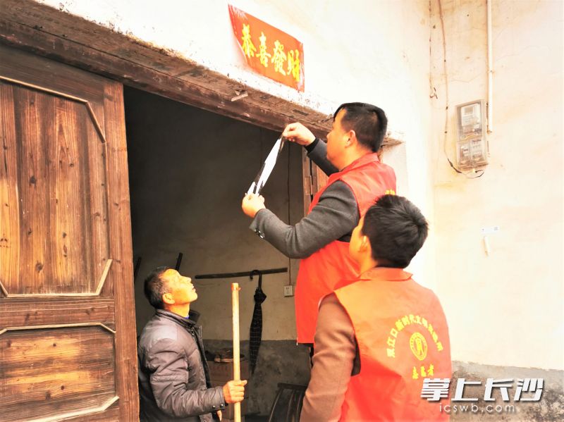 在走訪慰問當(dāng)中，雙江口鎮(zhèn)黨員干部為鄉(xiāng)親家貼上春聯(lián),。均為受訪方供圖