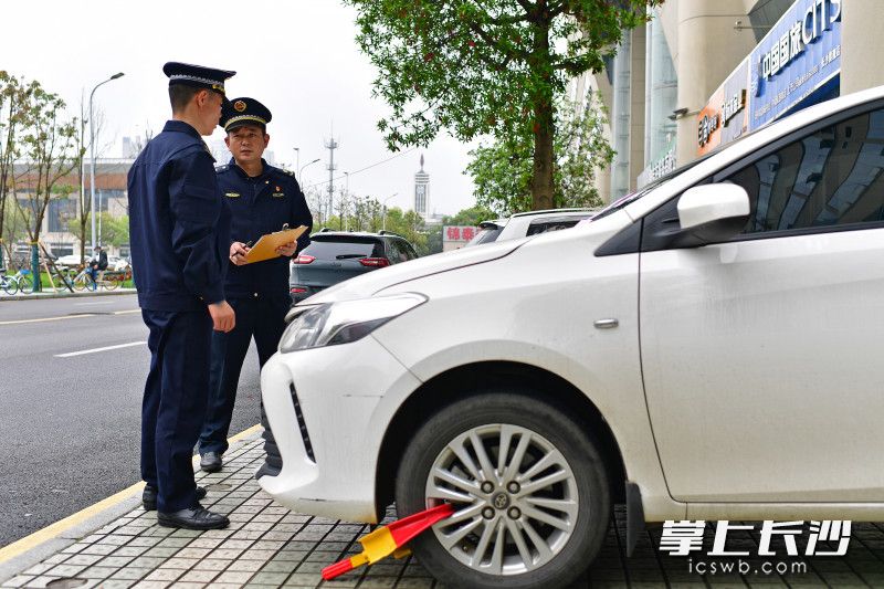 在錦泰廣場,，芙蓉區(qū)行政執(zhí)法大隊城管執(zhí)法人員對人行道違停車輛進行處罰,。