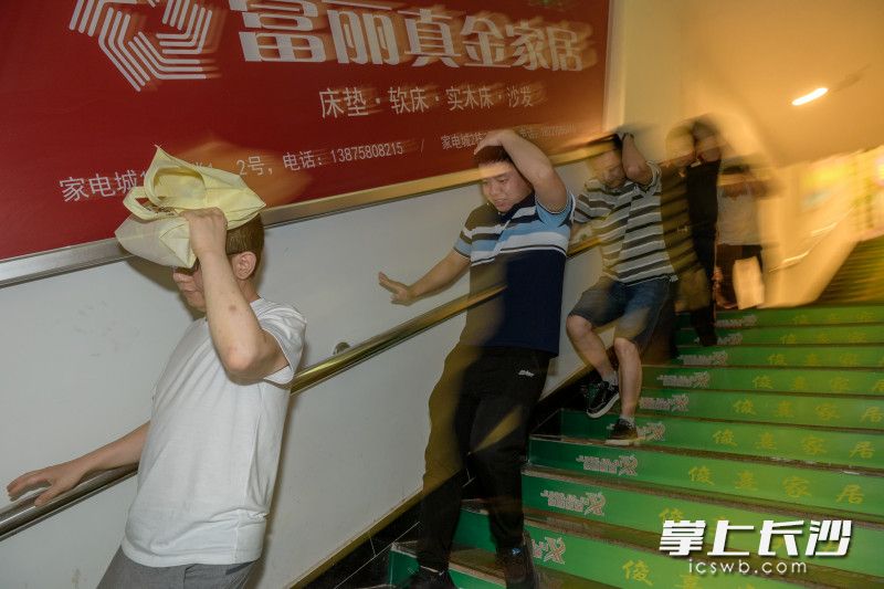 地震緊急疏散演練現(xiàn)場,，伴隨著尖利的警報聲響起，三湘大市場家電城放心購物街內(nèi)的數(shù)十位居民群眾立刻有序地護(hù)頭沿著扶梯下樓撤離,。長沙晚報全媒體記者 陳飛 攝