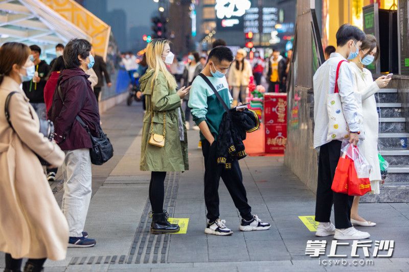 在長(zhǎng)沙黃興南路步行商業(yè)街上，幾位路人戴著口罩正在排隊(duì)買小吃,。全媒體記者 董陽(yáng) 攝
