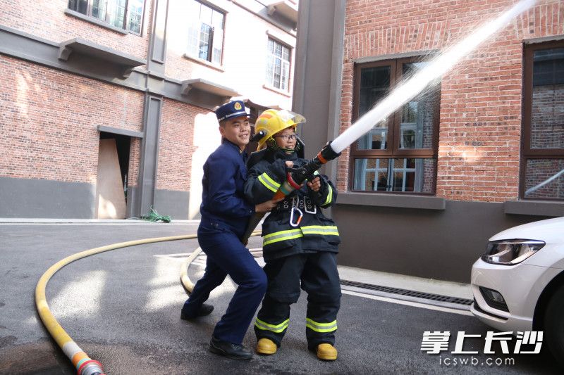 小朋友穿上滅火防護服,，與消防員一起使用消防水槍“滅火”,。