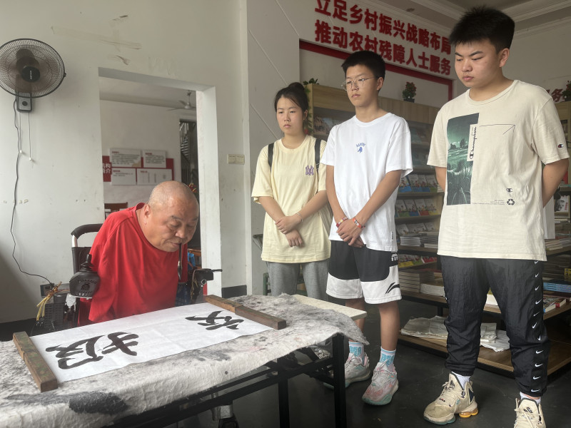 “半截人”周國民用嘴叼筆，給兩位“準大學(xué)生”（右一、右三）寫下“報效祖國”的青春寄語。  均為長沙晚報全媒體記者 黎鐵橋 攝