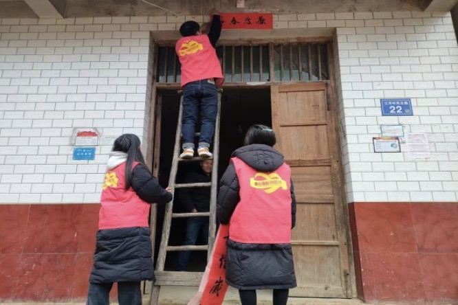 志愿者為困難群眾貼對聯(lián)。