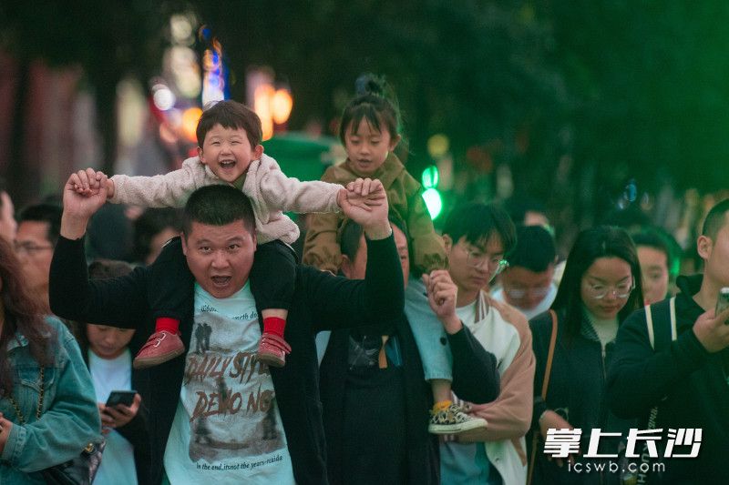 一位家長背著小孩在長沙街頭快樂“飛翔”,。