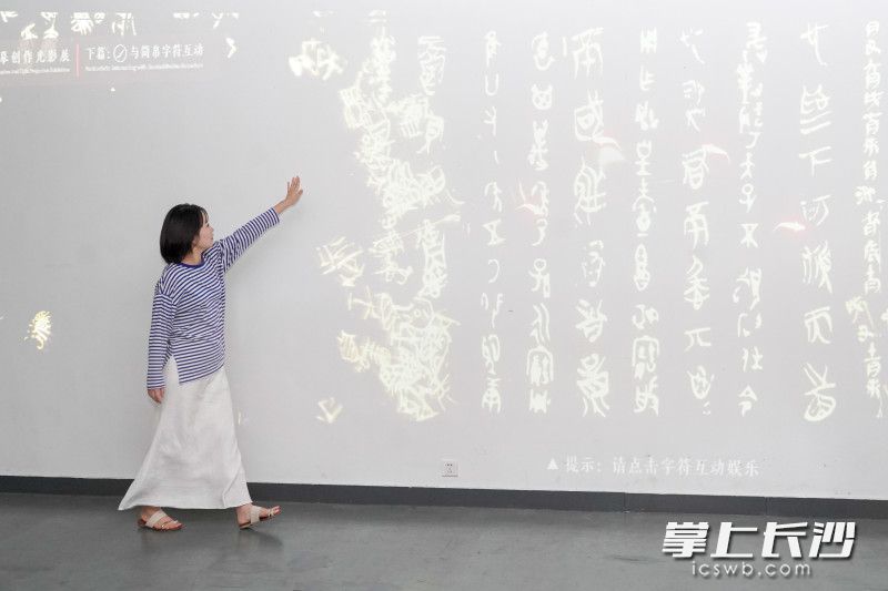 一位游客伸手掠過(guò)《溯源書法文脈,，推進(jìn)文化自信——中國(guó)簡(jiǎn)帛書法藝術(shù)臨摹創(chuàng)作光影展》屏幕，屏幕文字隨即產(chǎn)生交互,，飛散飄揚(yáng),，十分生動(dòng)。
