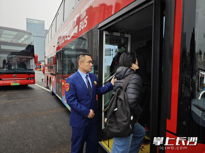 駕駛員匡飛鴿站在等候發(fā)車的巴士門前，熱情迎接游客,。