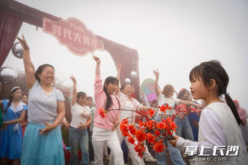 現(xiàn)場一位小女孩手捧著杜鵑花，津津有味地欣賞著“時(shí)代大舞廳”里大家的即興舞蹈,。