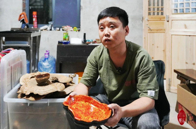 王鑫手捧著做好的大漆靈芝盤,，在他的右手邊是還未進行加工的靈芝。