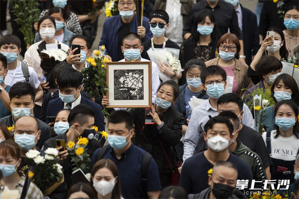 5月24日,，一位手舉著袁老剪紙的市民排隊進入殯儀館緬懷袁老。